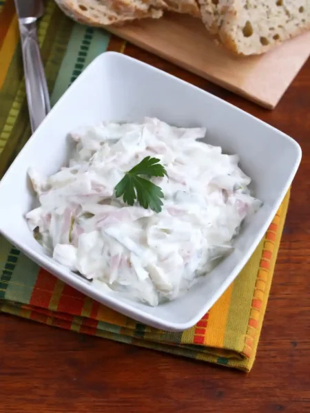 Omas fleischsalat rezept mit mayonnaise in einer Schüssel serviert mit Brot im Hintergrund