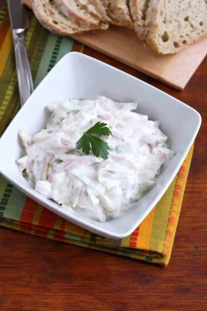 Omas fleischsalat rezept mit mayonnaise in einer Schüssel serviert mit Brot im Hintergrund