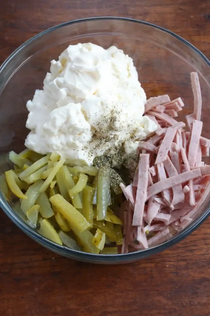 Fleischsalat zutaten in einer Schüssel mit mayonnaise, fleischwurst und gewürzgurken