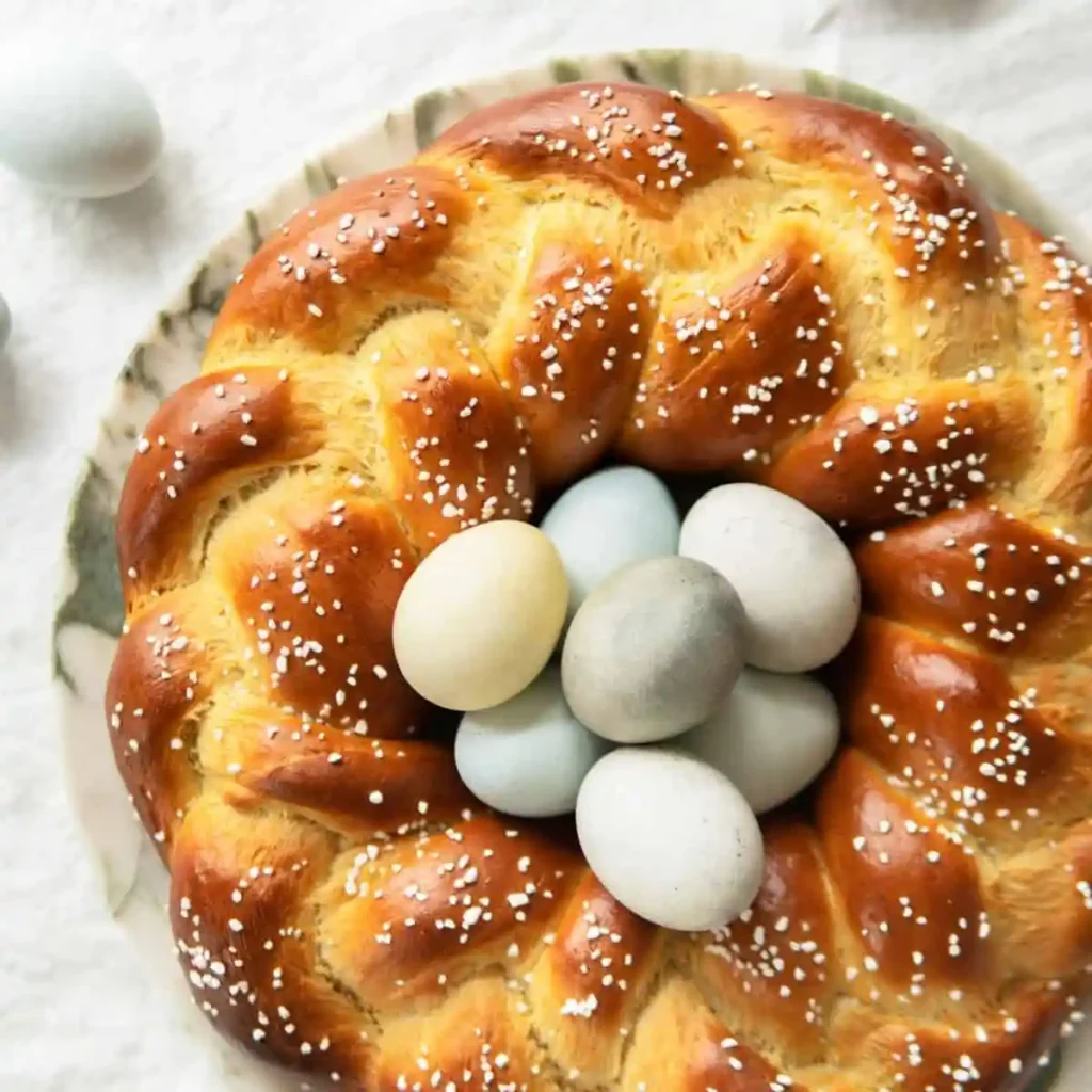 Osterkranz Rezept aus Hefeteig – goldbrauner geflochtener Osterkranz mit Hagelzucker und bunten Ostereiern in der Mitte wie Omas Osterkranz