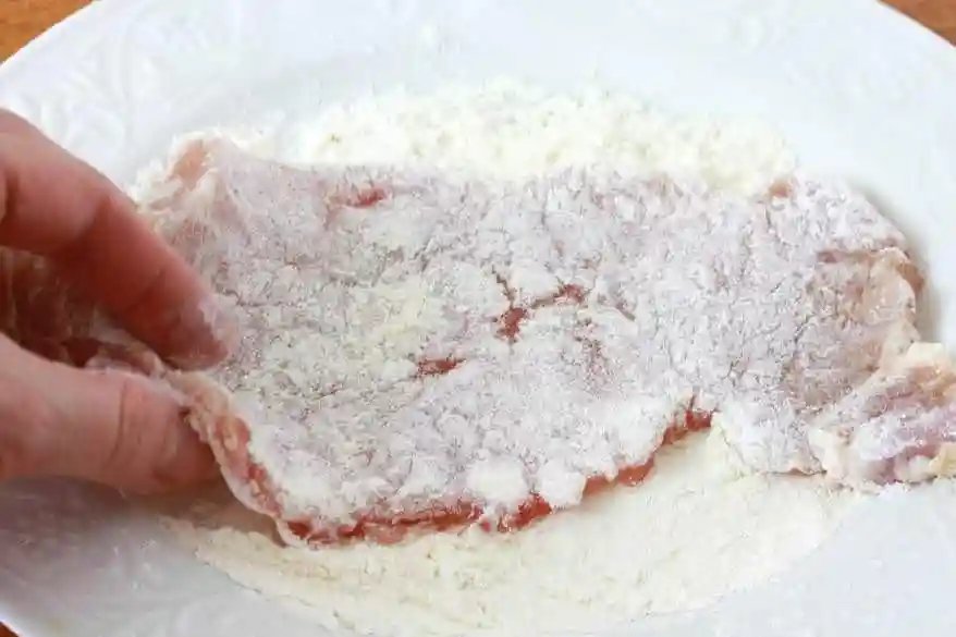 Schweineschnitzel in Mehl wenden – erster Schritt der Schnitzel panieren Reihenfolge für ein klassisches Schnitzel Rezept