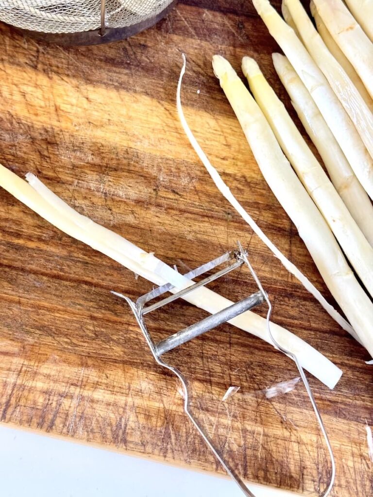 Weißer Spargel schälen mit Sparschäler auf Holzbrett – Spargel zubereiten und Spargel richtig kochen