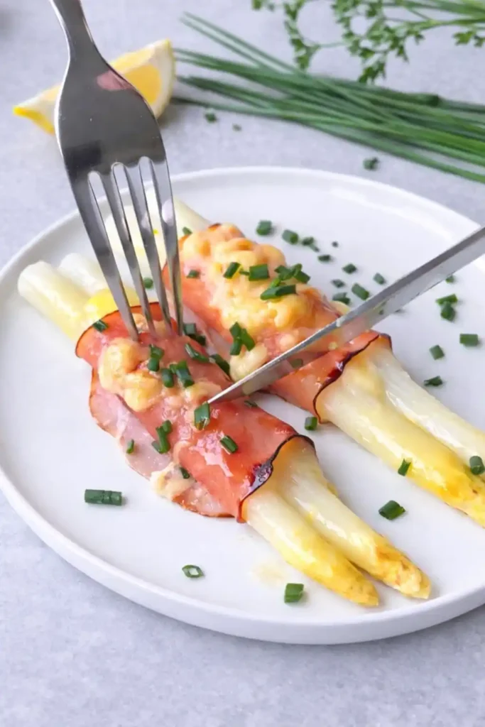 Spargel überbacken mit Schinken und Käse serviert – Spargel Schinkenröllchen auf Teller mit Gabel
