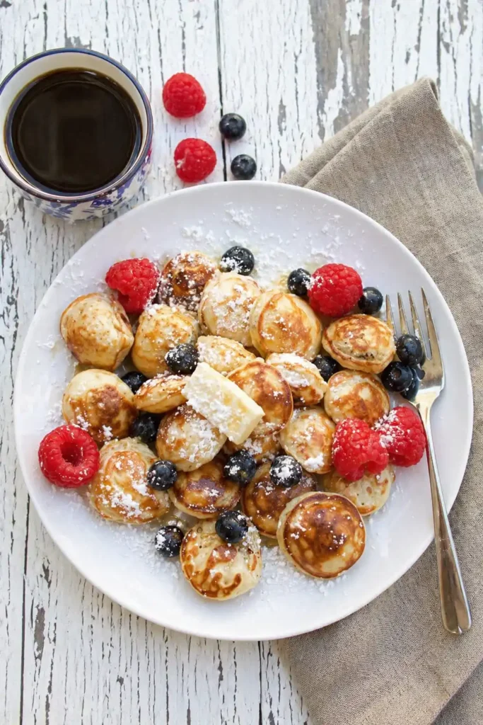 Holländische Poffertjes mit Butter, Puderzucker, Himbeeren und Blaubeeren nach original Poffertjes Rezept serviert