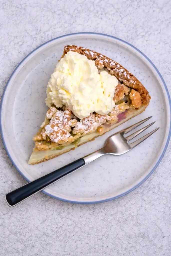 Rhabarberkuchen mit Pudding und Streusel Stück mit Sahne auf Teller – saftiger Rhabarberkuchen nach Omas Rezept