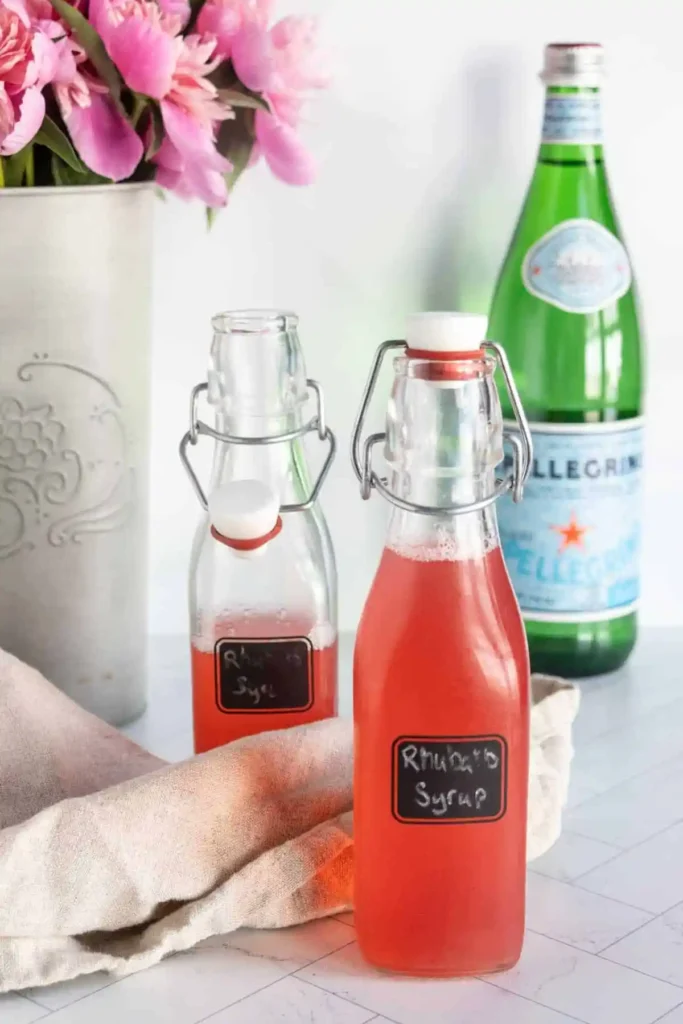 Rhabarbersirup selber machen – hausgemachter Rhabarber Sirup in Glasflaschen mit Sprudelwasser im Hintergrund