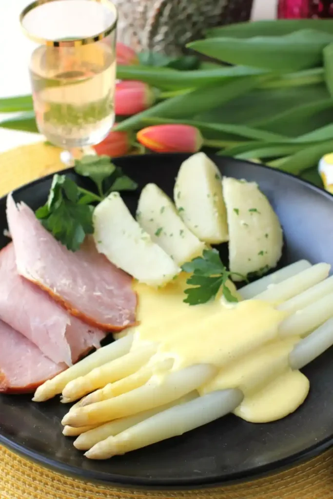 Spargel mit Sauce Hollandaise auf dem Teller – weißer Spargel mit Schinken, Kartoffeln und cremiger Soße zu Spargel