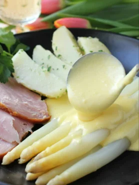 Spargel mit Sauce Hollandaise auf dem Teller – weiße Spargelstangen mit cremiger Soße zu Spargel, Kartoffeln und Schinken