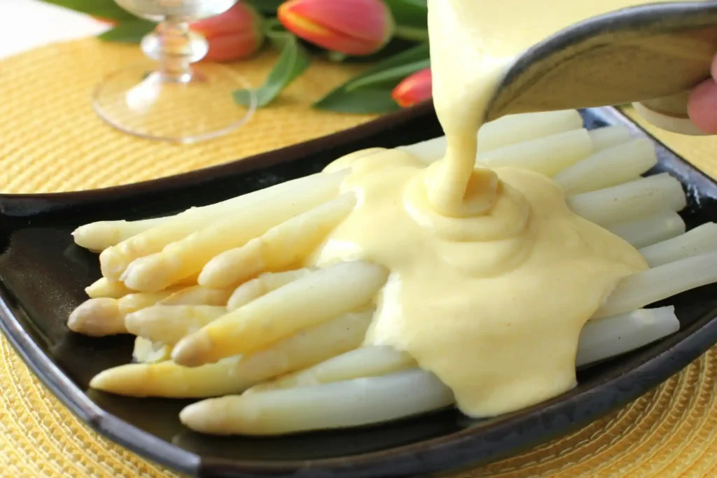 Spargel mit Sauce Hollandaise anrichten – cremige Soße zu Spargel wird über weißen Spargel gegossen