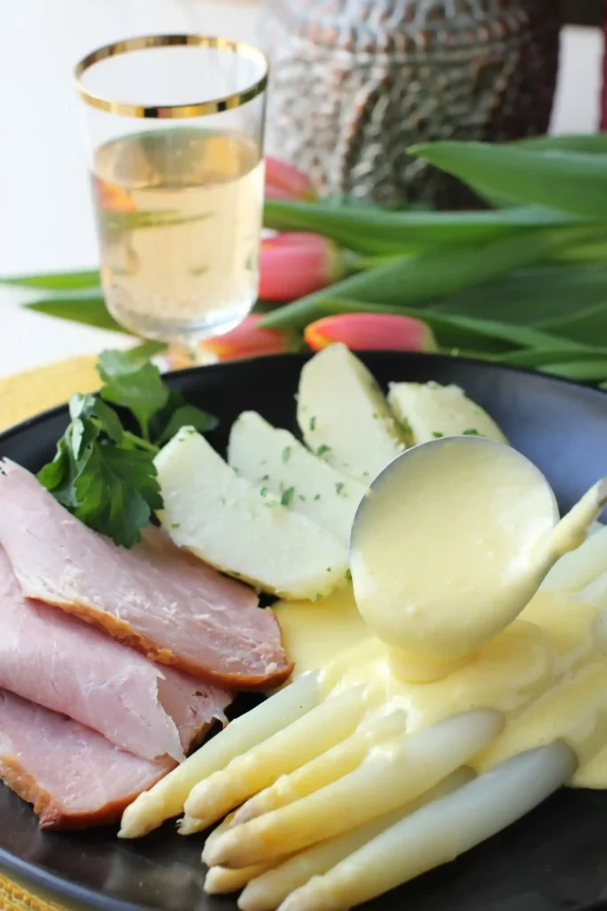 Spargel mit Sauce Hollandaise auf dem Teller – weiße Spargelstangen mit Schinken, Kartoffeln und cremiger Soße zu Spargel