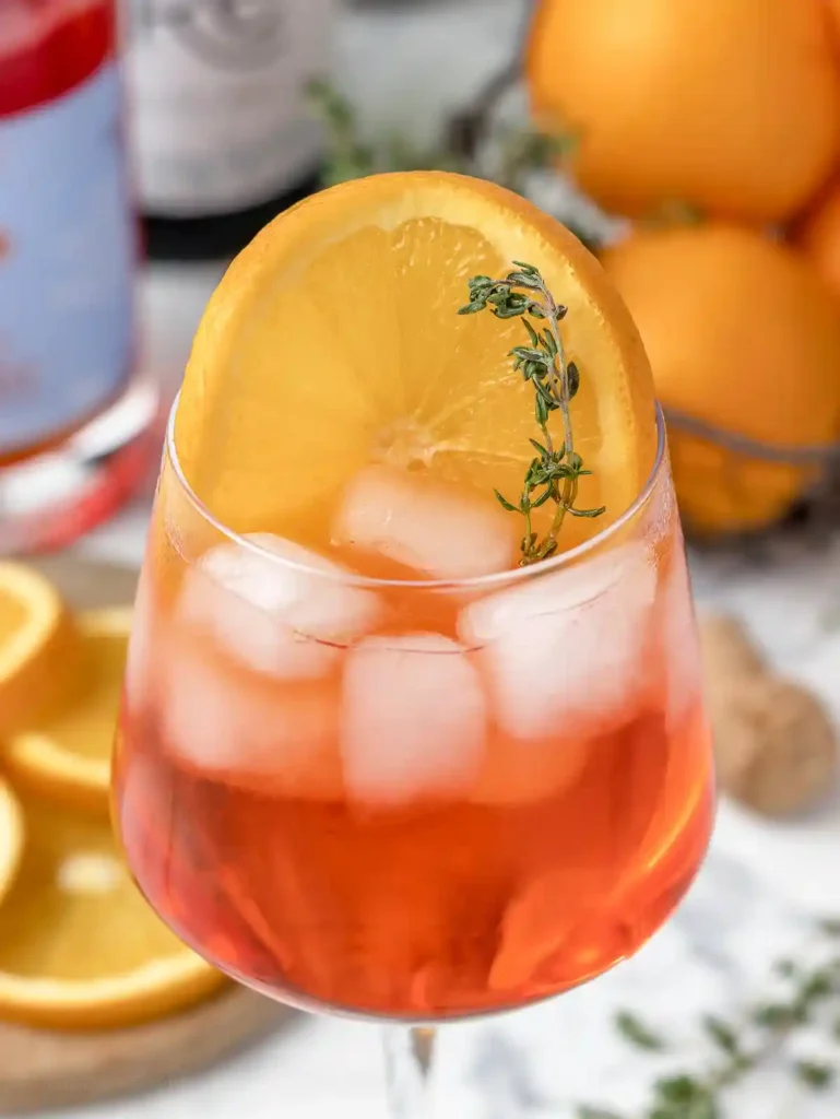 Aperol Spritz ohne Alkohol Nahaufnahme mit Orangenscheibe, Eiswürfeln, Thymian und alkoholfreiem Aperol