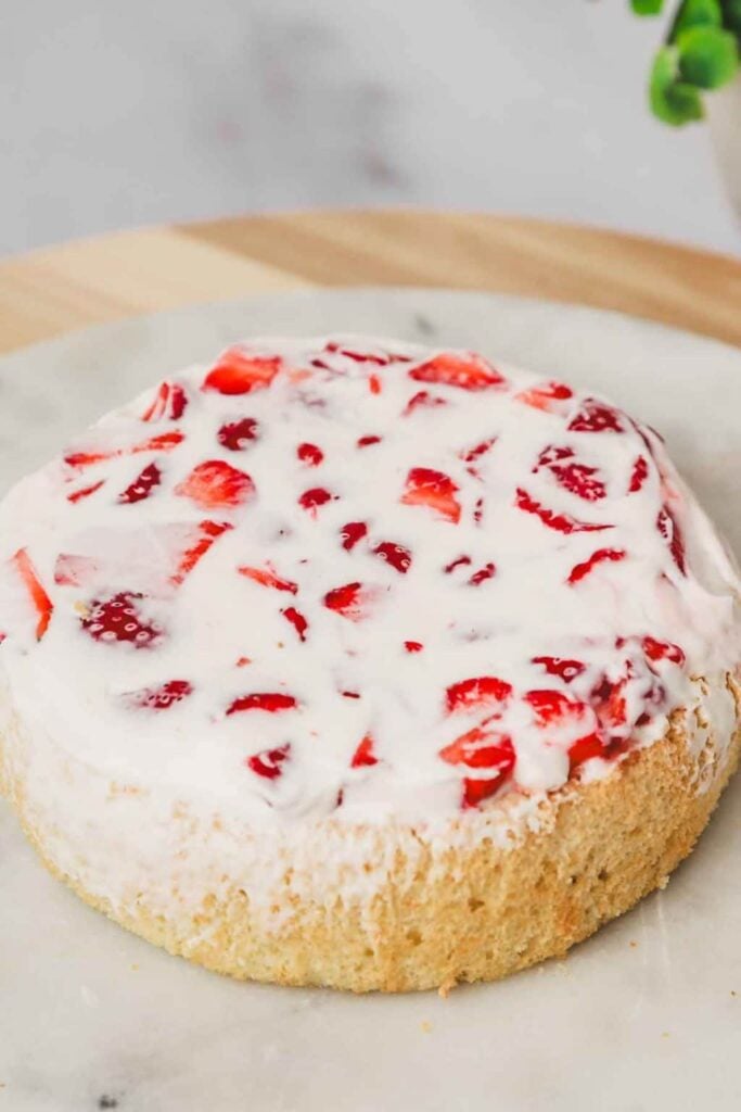 Erdbeertorte mit Sahne beim Schichten mit Erdbeercreme und frischen Erdbeeren auf luftigem Tortenboden