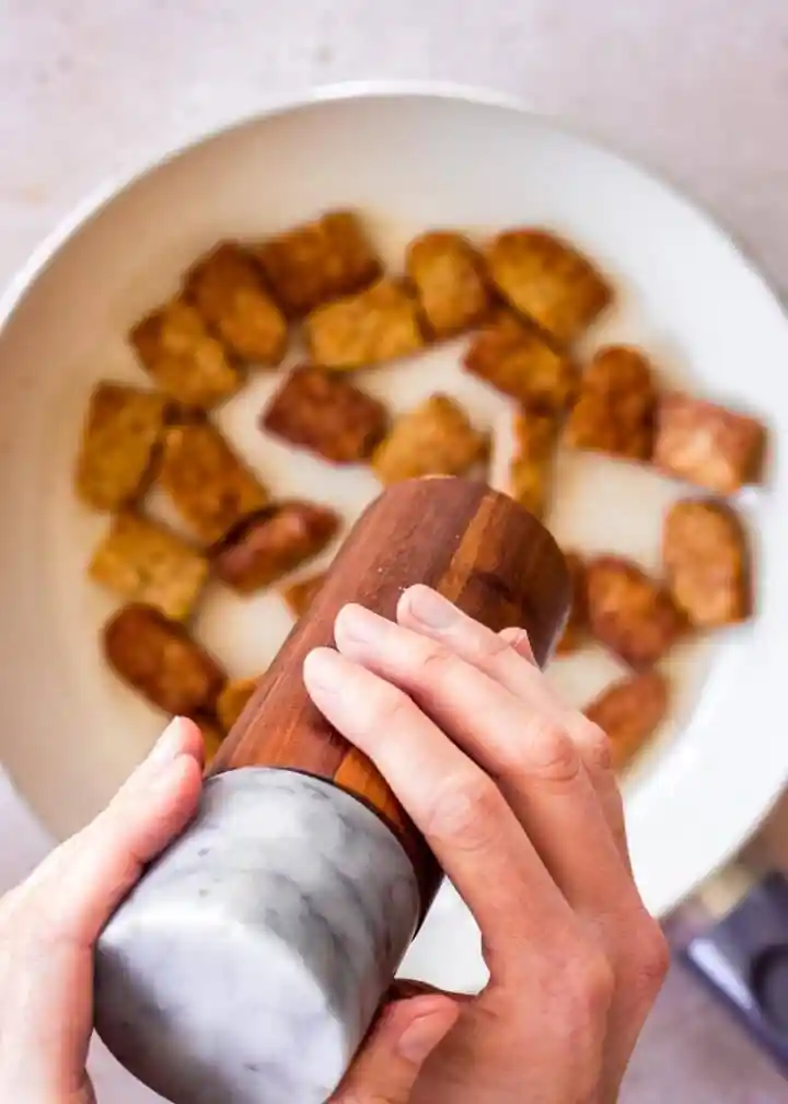 Tempeh würzen beim Braten mit Salz und Pfeffer in der Pfanne als einfaches Tempeh Rezept