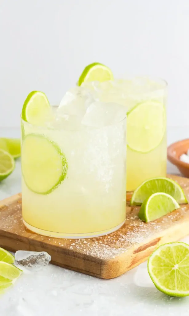 Alkoholfreie Margarita mit Limette, Eiswürfeln und Salzrand auf einem Holzbrett