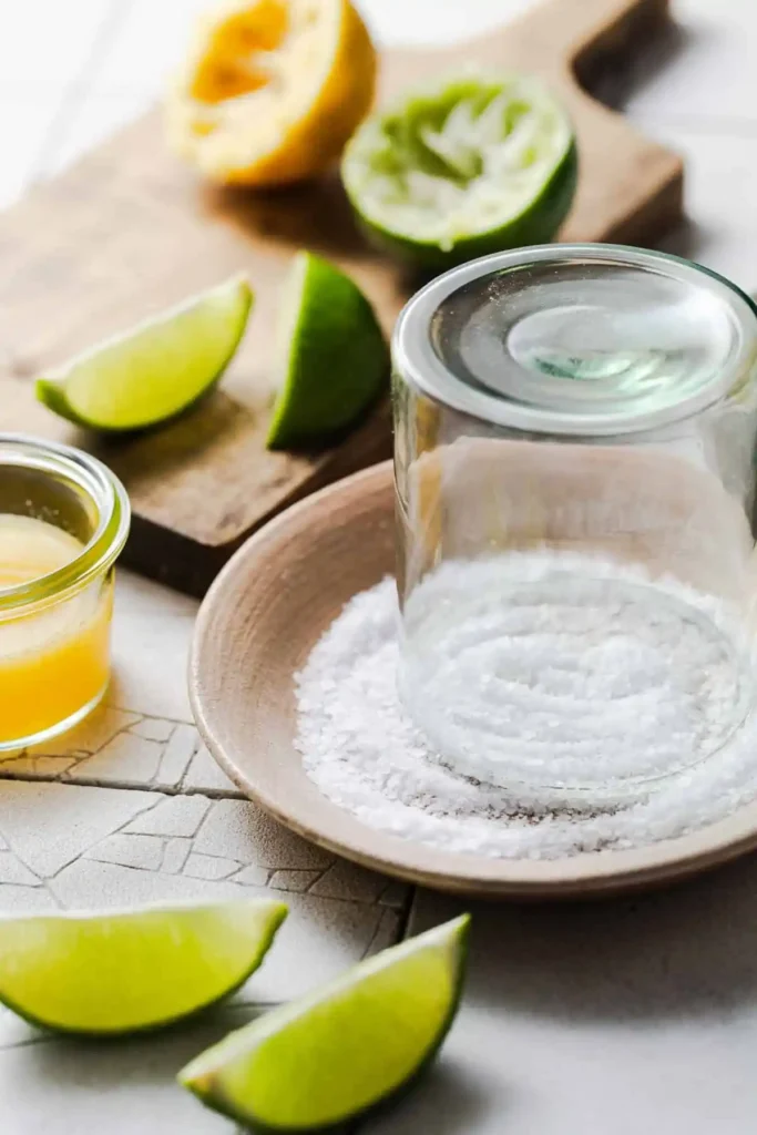 Glasrand für Margarita ohne Alkohol wird in grobes Salz gedrückt, daneben liegen frische Limettenspalten
