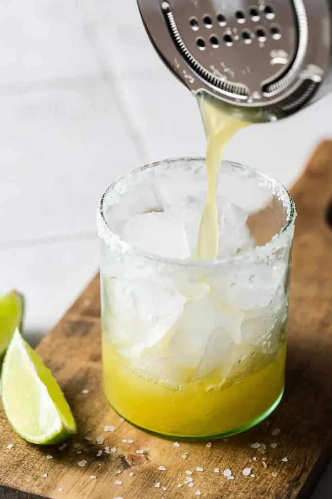 Alkoholfreie Margarita wird durch ein Barsieb in ein Glas mit Eiswürfeln und Salzrand gegossen