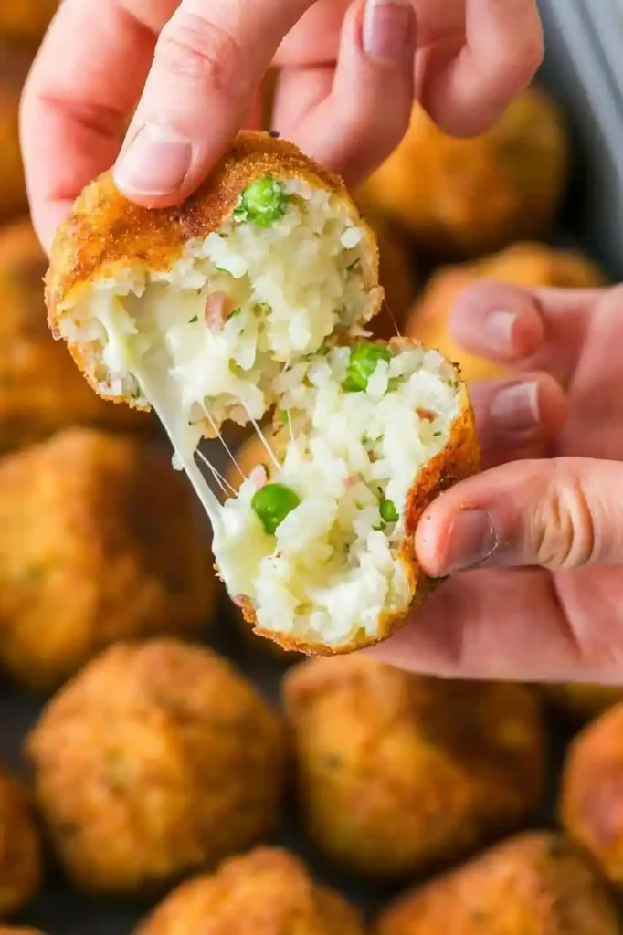 Geöffnetes Arancini mit geschmolzener Mozzarella-Füllung, Reis, Erbsen und Schinken vor goldbraunen sizilianischen Reisbällchen