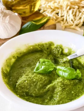 Selbst gemachtes grünes Basilikum-Pesto Genovese in einer weißen Schale mit frischen Basilikumblättern, Knoblauch, Olivenöl und Pasta.