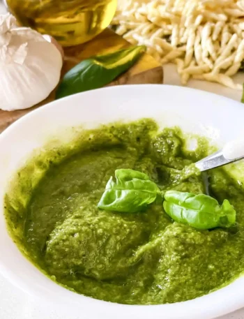 Selbst gemachtes grünes Basilikum-Pesto Genovese in einer weißen Schale mit frischen Basilikumblättern, Knoblauch, Olivenöl und Pasta.
