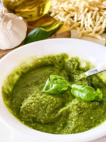 Selbst gemachtes grünes Basilikum-Pesto Genovese in einer weißen Schale mit frischen Basilikumblättern, Knoblauch, Olivenöl und Pasta.