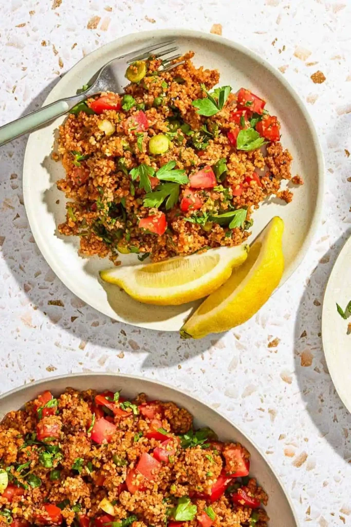 Türkischer Bulgursalat Kısır mit Tomaten, Petersilie, Frühlingszwiebeln und Zitronenspalten auf einem Teller