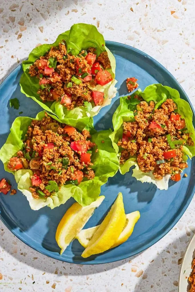 Türkischer Bulgursalat Kısır mit Tomaten und Petersilie, serviert in knackigen Salatblättern mit Zitronenspalten