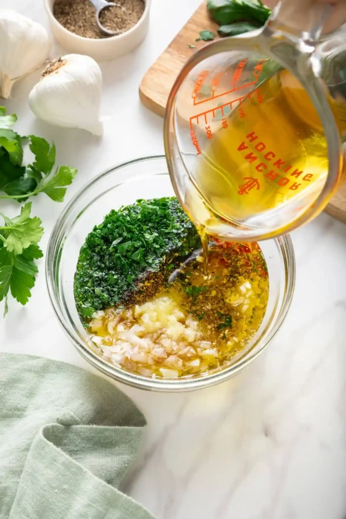 Olivenöl wird zu Petersilie, Knoblauch, Schalotte, Oregano und Chili für eine argentinische Chimichurri-Sauce gegeben
