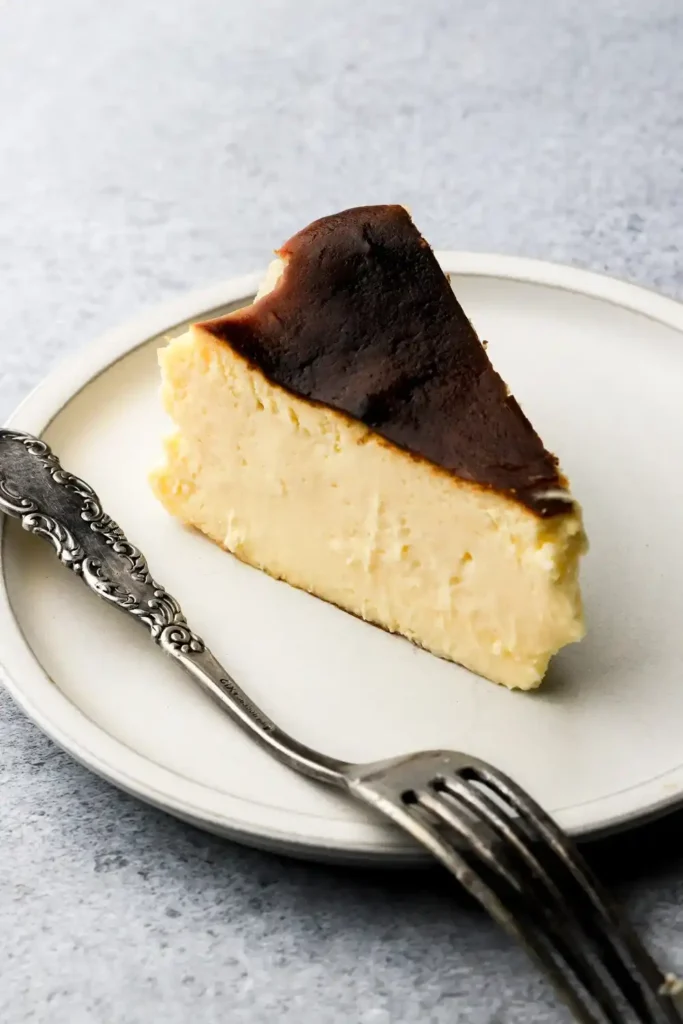 Stück San Sebastian Cheesecake nach Original-Rezept mit dunkler Oberfläche und cremiger Mitte auf einem weißen Teller