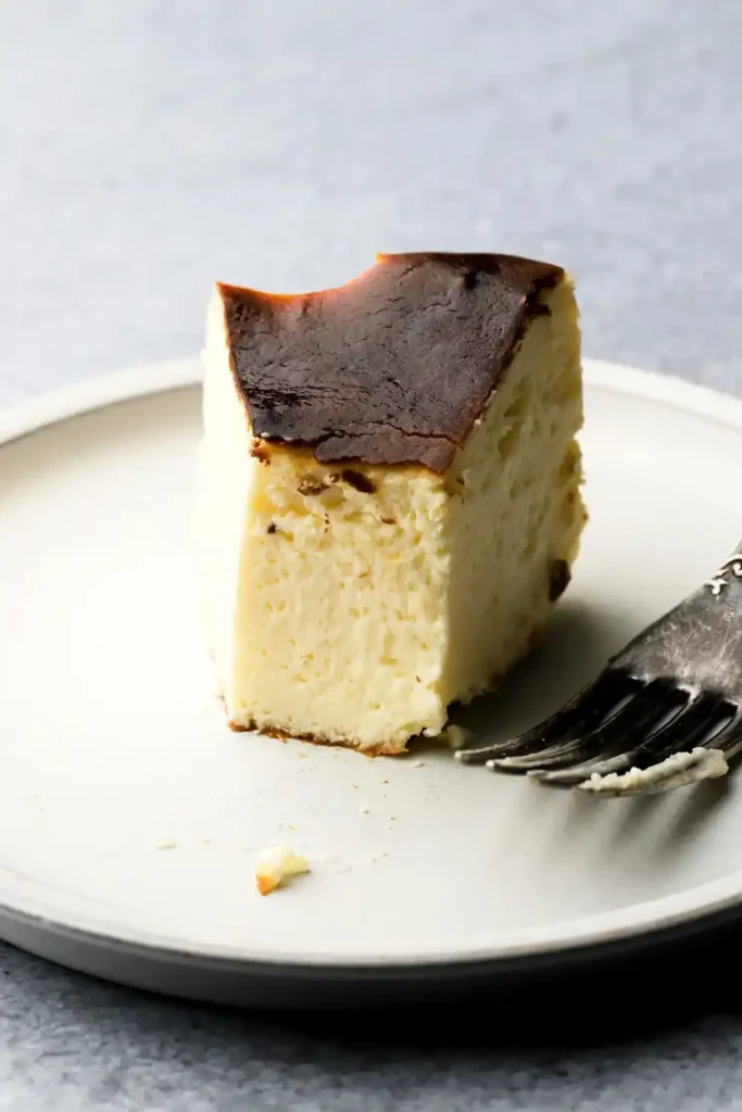 Stück San Sebastian Cheesecake mit dunkler Kruste und cremiger Mitte auf weißem Teller