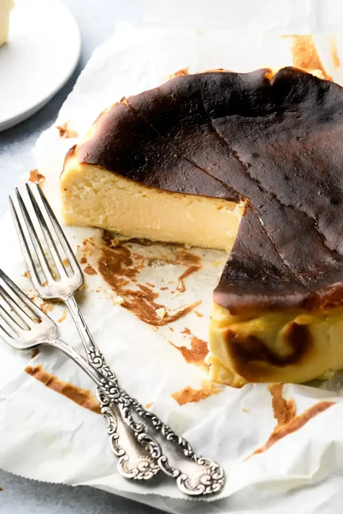 Angeschnittener San Sebastian Cheesecake mit dunkler Kruste, cremiger Mitte und zwei Kuchengabeln
