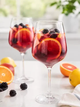 Sangria ohne Alkohol in Weingläsern mit Orangenscheiben, Apfelstücken und Brombeeren