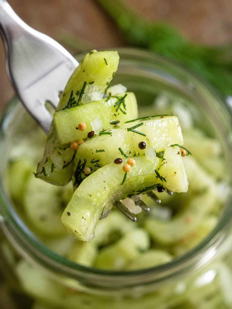 Schüttelgurken mit Zwiebeln, Dill und Senfkörnern auf einer Gabel über einem Glas