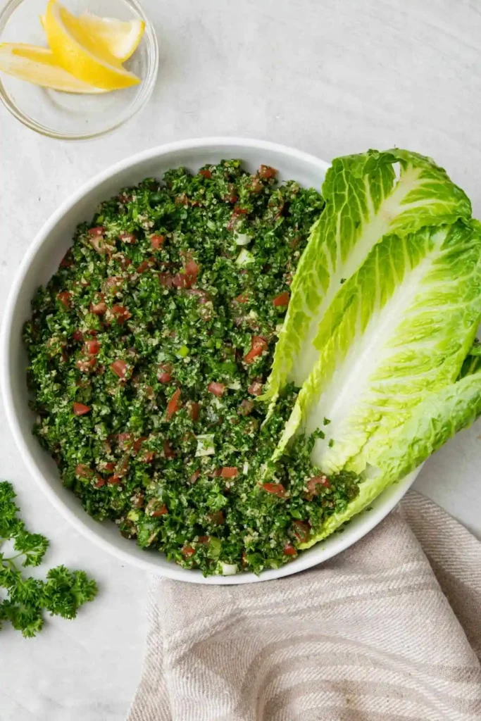 Libanesischer Tabouleh-Salat mit Petersilie, Tomaten und Bulgur, serviert mit Römersalat und Zitronenspalten