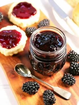 Selbst gemachte Brombeermarmelade ohne Kerne im Glas mit frischen Brombeeren, Löffel und bestrichenen Scones.