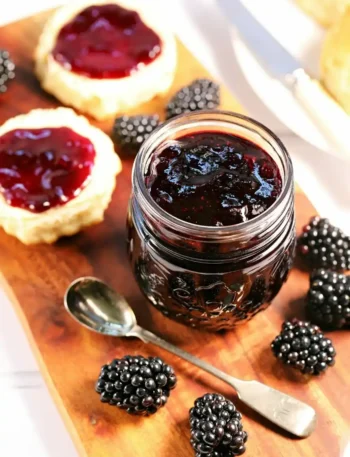 Selbst gemachte Brombeermarmelade ohne Kerne im Glas mit frischen Brombeeren, Löffel und bestrichenen Scones.