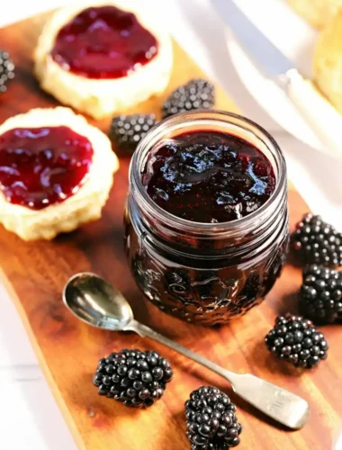 Selbst gemachte Brombeermarmelade ohne Kerne im Glas mit frischen Brombeeren, Löffel und bestrichenen Scones.