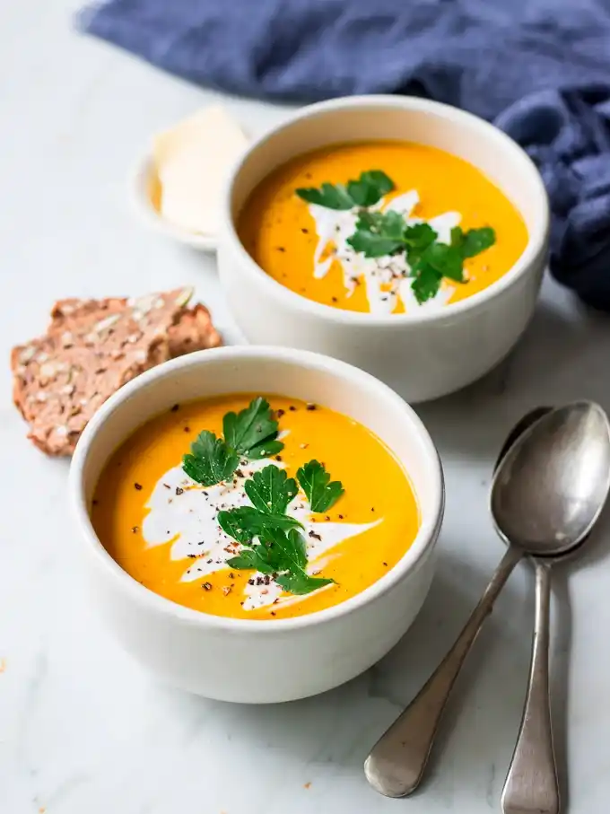 Zwei Schalen orangefarbene Hokkaido-Kürbissuppe mit Kokosmilch, Petersilie und schwarzem Pfeffer, dazu Körnerbrot.