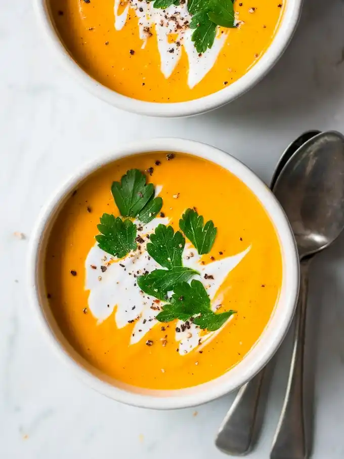 Nahaufnahme von cremiger Hokkaido-Kürbissuppe mit Kokosmilch, frischer Petersilie und schwarzem Pfeffer.