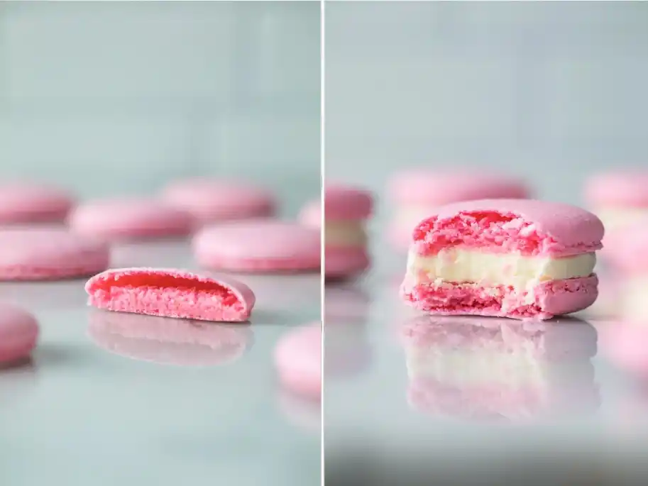 Aufgeschnittene rosa Macaron-Schale und gefülltes französisches Macaron mit heller Cremefüllung in der Nahaufnahme.
