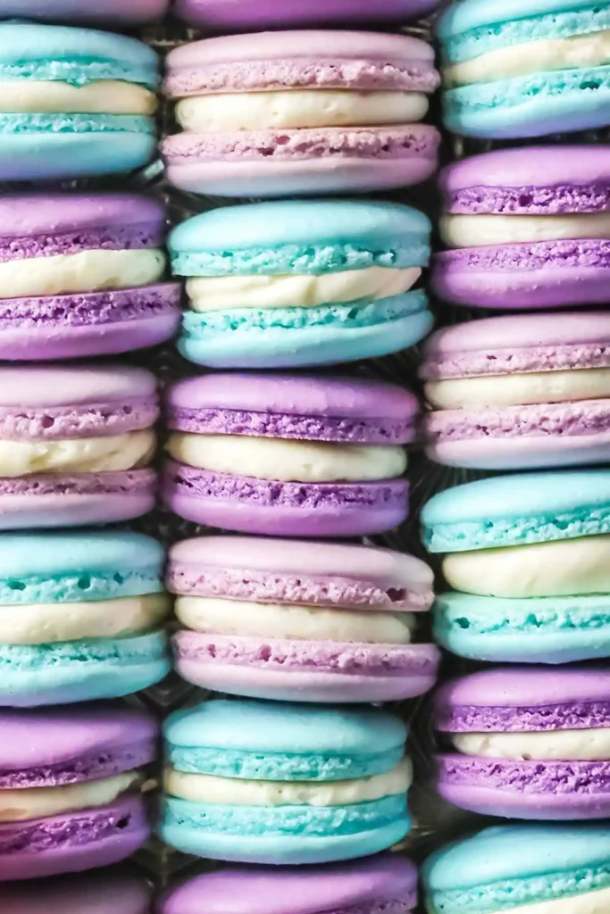 Nahaufnahme von türkisen, lilafarbenen und rosafarbenen französischen Macarons mit heller Cremefüllung und typischen Füßchen.