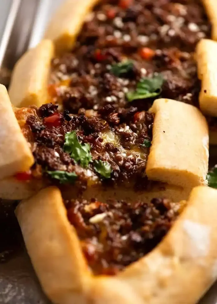 Nahaufnahme einer aufgeschnittenen Kıymalı Pide mit würziger Lammhackfüllung, Käse, Sesam und frischen Kräutern.