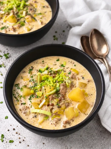 Käse-Lauch-Suppe mit Schmelzkäse, Hackfleisch und Kartoffeln in schwarzen Schüsseln