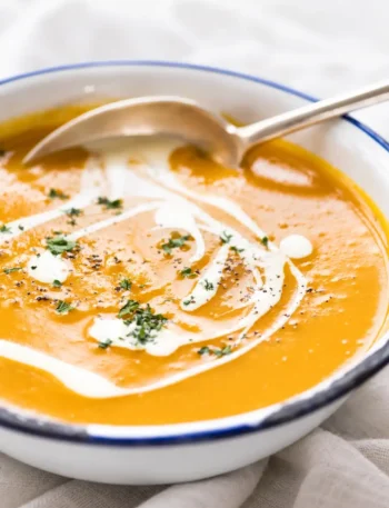 Cremige Kürbiscremesuppe mit Sahne, Petersilie und Pfeffer in einer weißen Schüssel