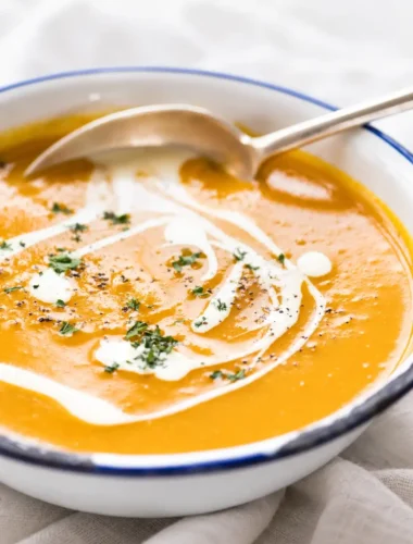 Cremige Kürbiscremesuppe mit Sahne, Petersilie und Pfeffer in einer weißen Schüssel