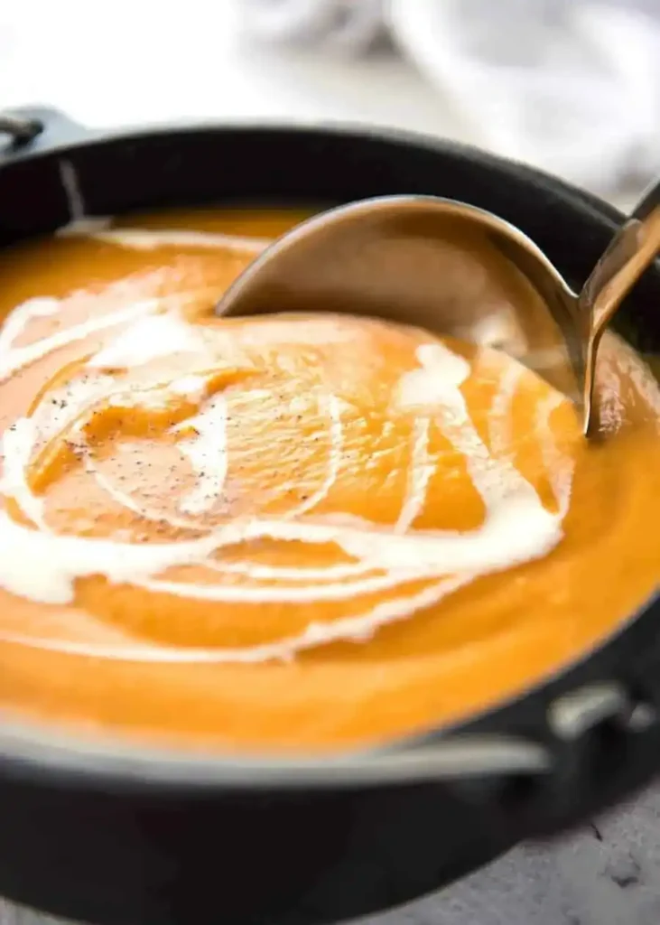Cremige Kürbiscremesuppe mit Sahne und Pfeffer in einem schwarzen Topf mit Suppenkelle