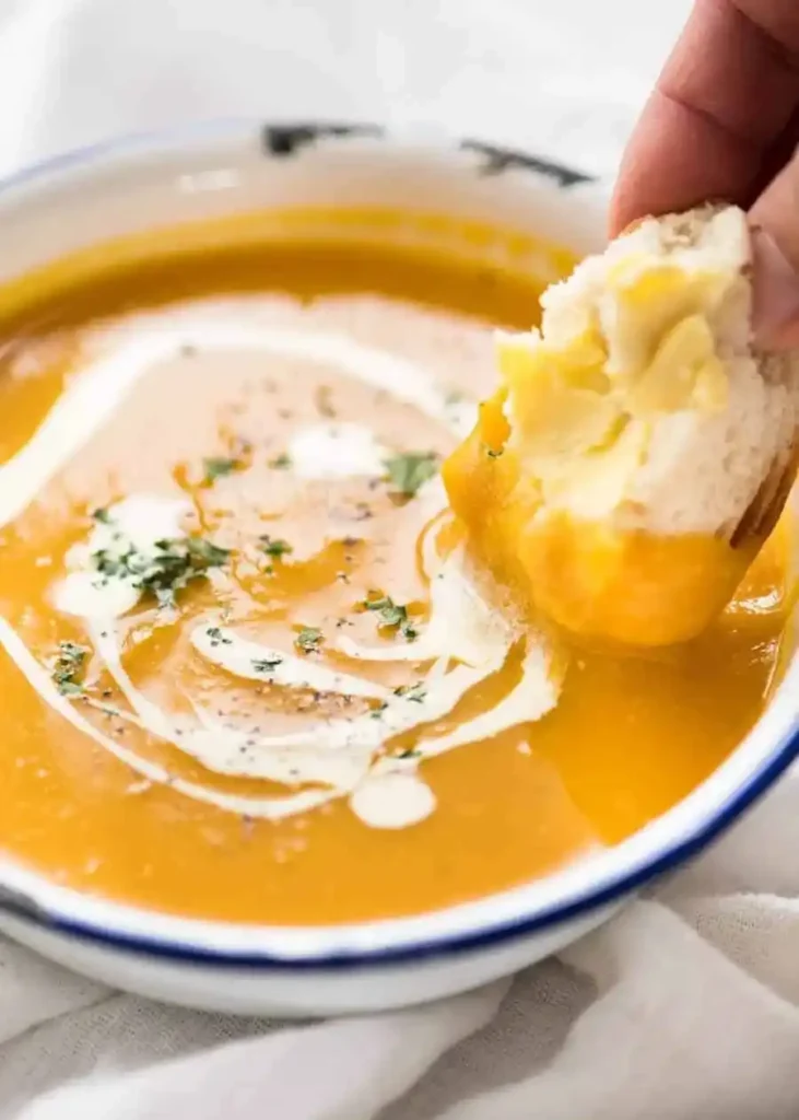 Butterbrot wird in cremige Kürbiscremesuppe mit Sahne und Kräutern getunkt
