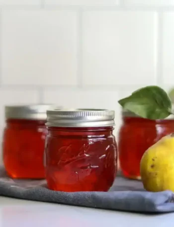 Drei Gläser mit rotem Quittengelee aus Saft neben einer frischen gelben Quitte