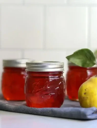 Drei Gläser mit rotem Quittengelee aus Saft neben einer frischen gelben Quitte