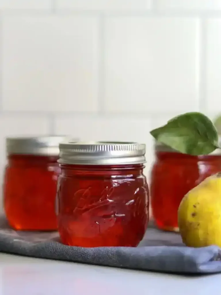Drei Gläser mit rotem Quittengelee aus Saft neben einer frischen gelben Quitte