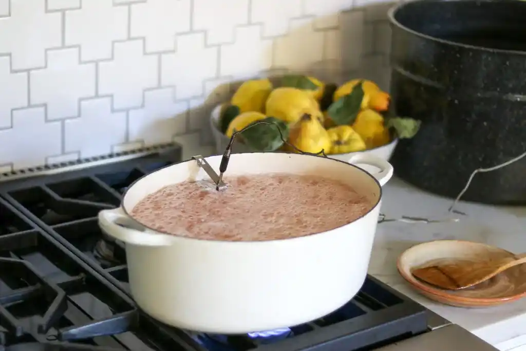 Quittengelee aus Saft kocht mit einem Thermometer in einem weißen Topf auf dem Gasherd